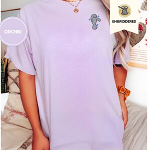 Person wearing an orchid Waving Manatee Embroidered T-Shirt