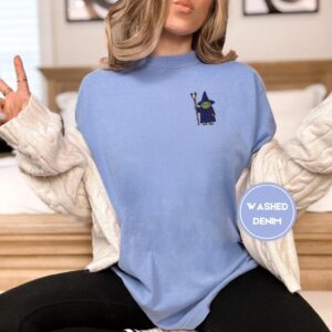 Person wearing a washed denim Wizard Frog with Staff Embroidered T-Shirt